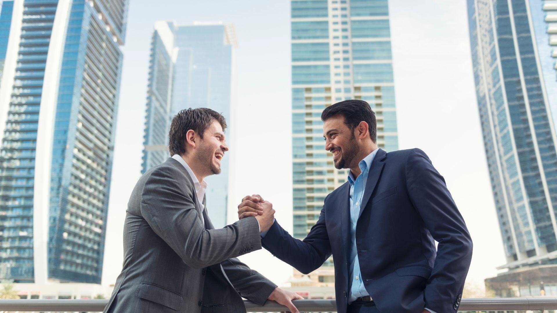 Two men shaking hands in front of high rise buildings