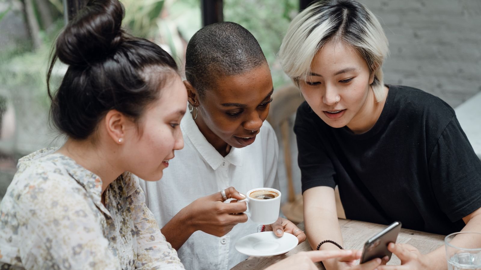 three ladies sitting together drinking coffee and looking at a smart phone