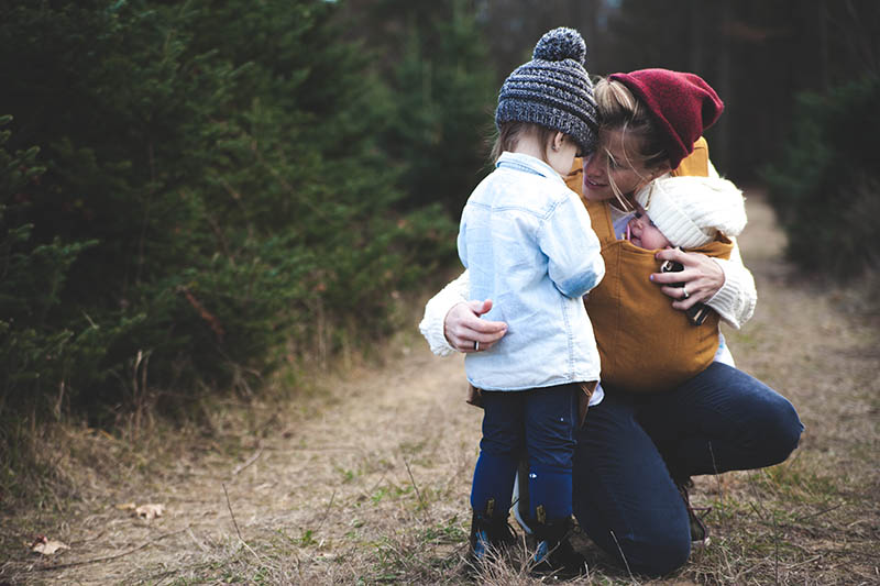 woman holding a baby while kneeling to comfort a young child